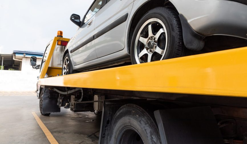 Broken down car on flatbed tow truck being transported to garage workshop for repair