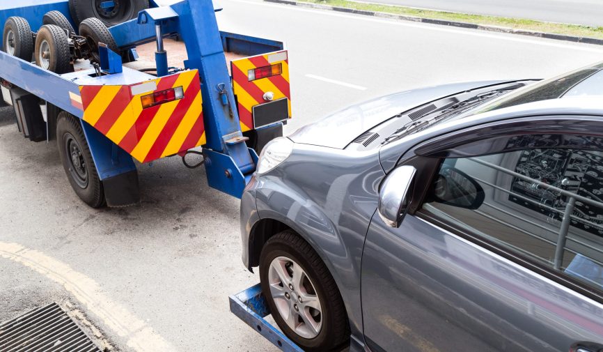 Tow truck towing a broken down car on the street.