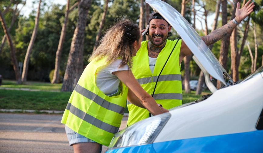Young tattooed couple in reflective safety vest calling for road assistance. Young tattooed couple in yellow reflective safety vest happy because someone is coming to help them after a car breakdown.