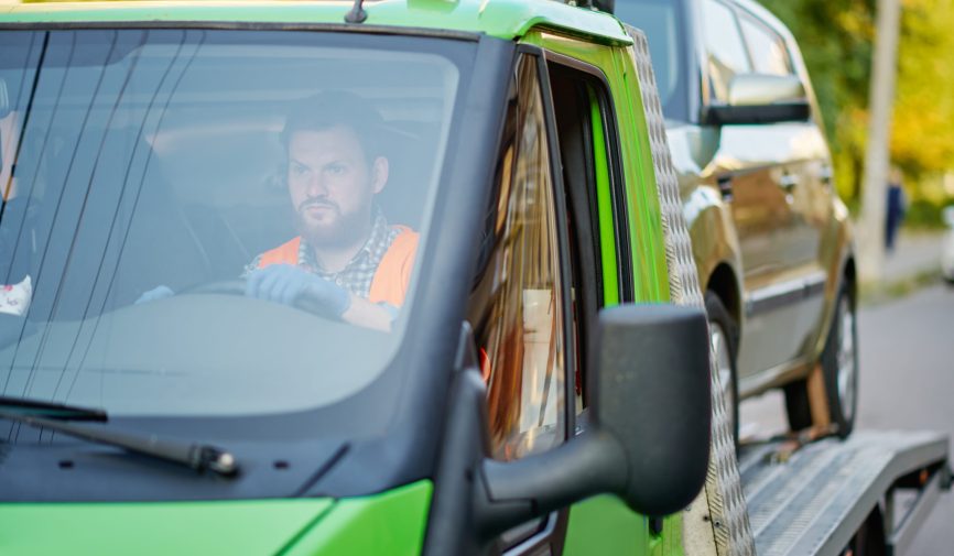 Man driving tow truck with car. Fast evacuation service. Closeup cropped image. Selective focus