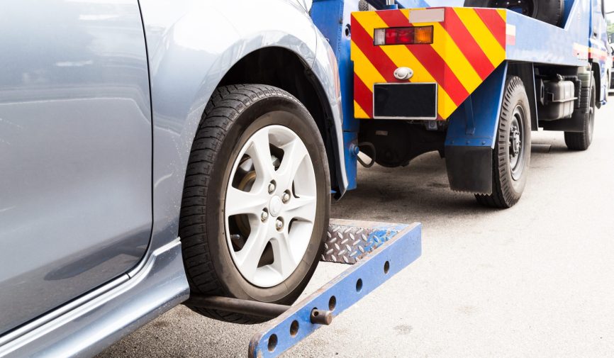 Tow truck towing a broken down car on the street.